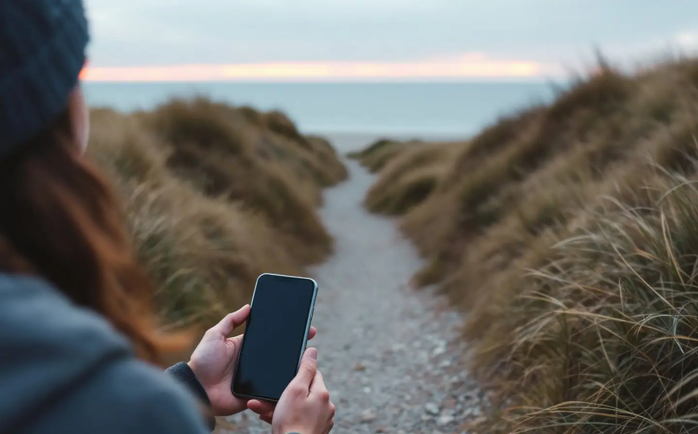 Small figure seen from behind walking a gravel path through grassy dunes at dusk
